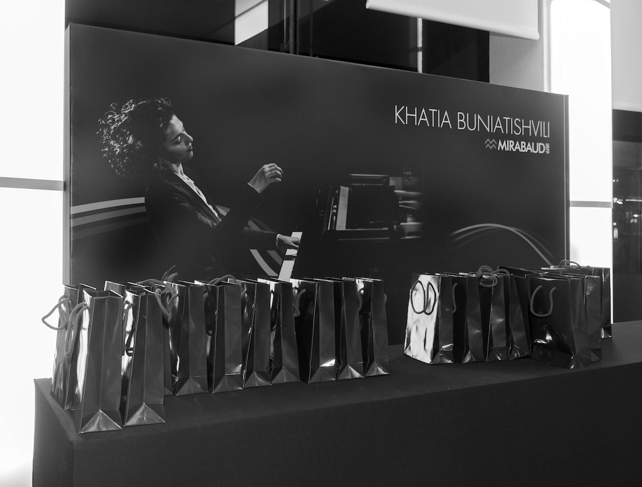 Photographie d'une table présentant des cadeaux pour les invités, avec l’affiche d’une pianiste en arrière-plan.